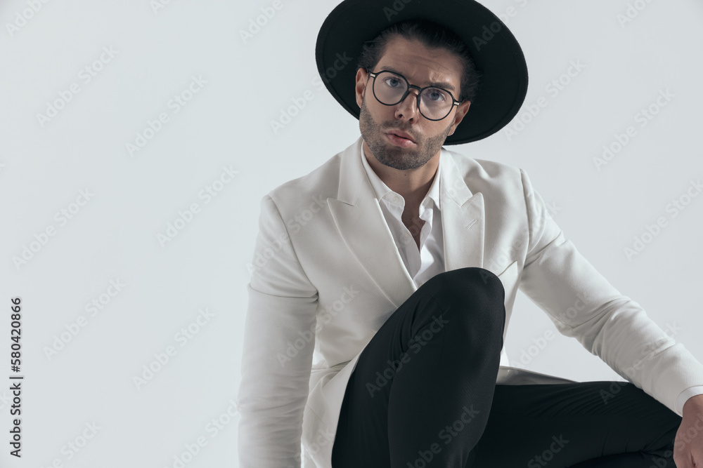 handsome young man with hat and glasses holding knee up and crouching handsome young man with hat and glasses holding knee up and crouching