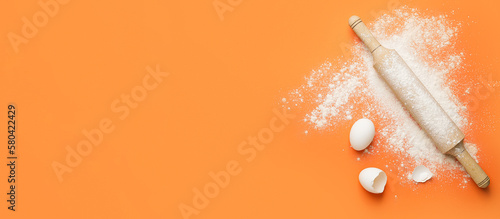 Rolling pin, flour and eggs on orange background with space for text