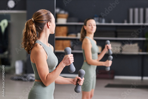 Girl looking at mirror while doing exercises with dumbbells in gym