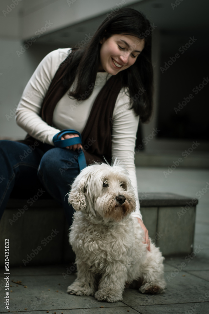 Smiling woman petting her dog in the city. Dog looking into the distance with its owner Smiling woman petting her dog in the city. Dog looking into the distance with its owner
