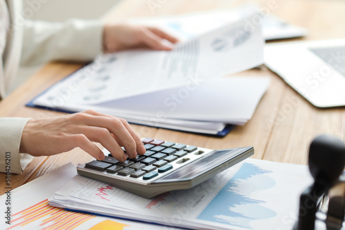 Fotografia Female accountant working with calculator and documents at table in office, clos