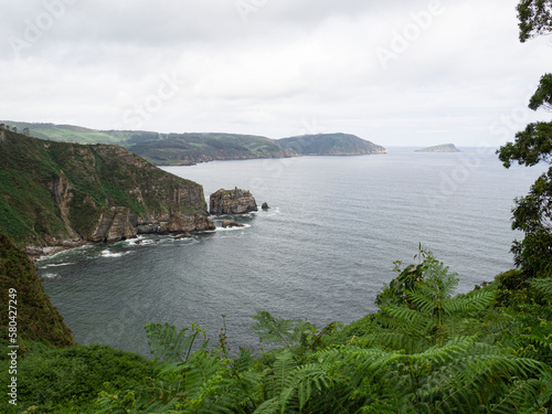 Vista panorámica del mar y la costa gallega desde un camino de la punta de Fociño do Porco en Lugo, con agua azul, montañas verdes, islotes y acantilados en un día nuboso de verano de 2021