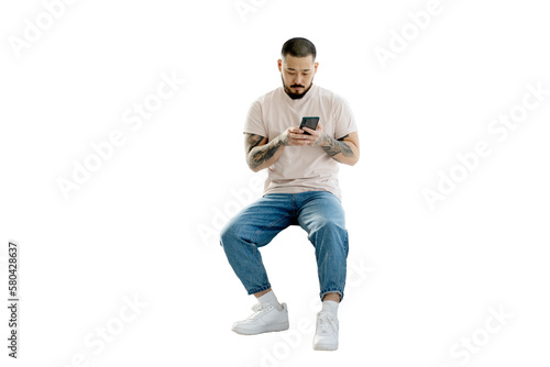 Serious handsome Korean man holding mobile phone shopping online isolated on transparent background. Young hipster guy with stylish tattoos on his hands chatting, reading text message. Clipping path  