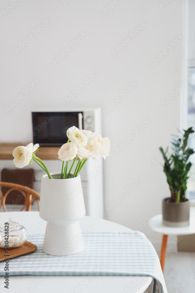 Vase with ranunculus flowers on dining table in kitchen Vase with ranunculus flowers on dining table in kitchen