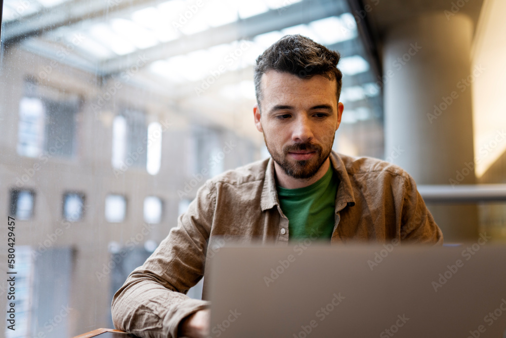 Portrait of pensive, handsome Latin student using laptop computer, Freelancer working in modern office. Attractive copywriter sitting at workplace. Successful business Portrait of pensive, handsome Latin student using laptop computer, Freelancer working in modern office. Attractive copywriter sitting at workplace. Successful business