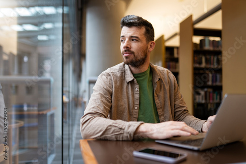 Portrait of attractive businessman, using laptop, hispanic man working online. Middle aged hipster guy working in modern office, looking away. Successful programmer sitting at desk