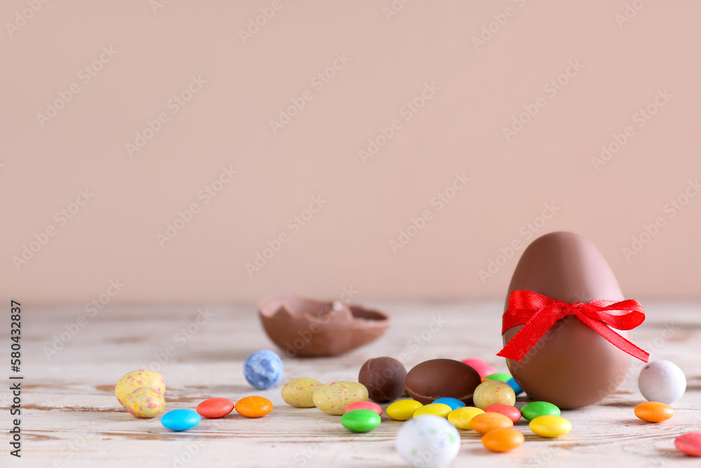 Chocolate Easter egg and candies on wooden table against brown background Chocolate Easter egg and candies on wooden table against brown background