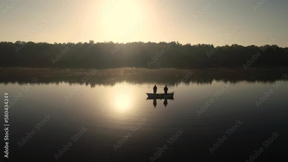 Aerial silhouette view of two anglers on a fishing boat it the middle of the lake. Two fishermen fishing at sunrise. Aerial silhouette view of two anglers on a fishing boat it the middle of the lake. Two fishermen fishing at sunrise.