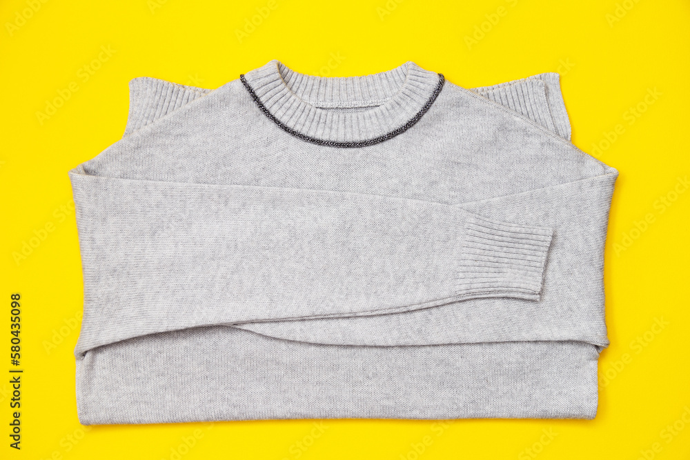 Knitted pullover in trendy grey color on yellow background, flay lay. Knitted pullover in trendy grey color on yellow background, flay lay.