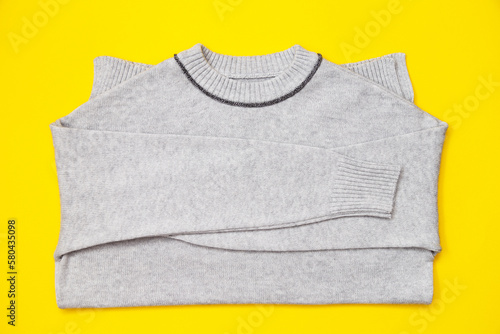 Knitted pullover in trendy grey color on yellow background, flay lay.