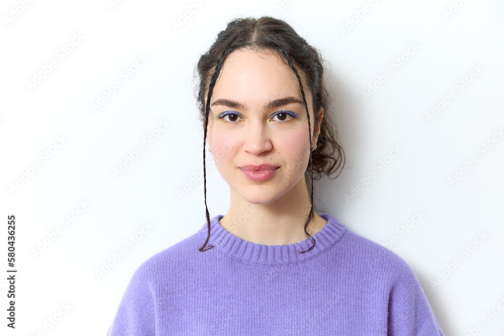 Studio shot of pretty female teenager with dark curly hair and pigtails wears purple sweater and blue and yellow eye shadow creative make-up on and looks at camera on grey copy space. Youth concept. Studio shot of pretty female teenager with dark curly hair and pigtails wears purple sweater and blue and yellow eye shadow creative make-up on and looks at camera on grey copy space. Youth concept.