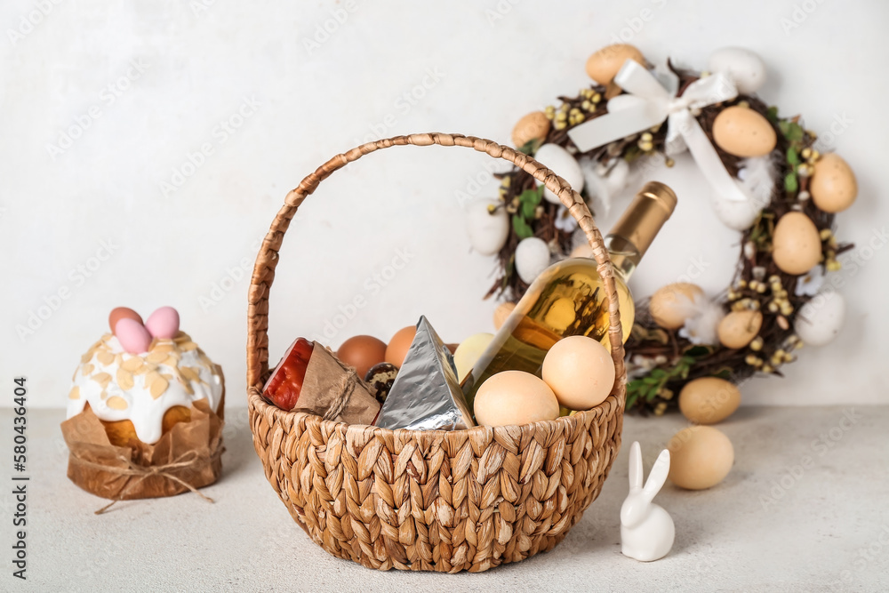 Basket with Easter eggs, bottle of wine and snacks on grey background