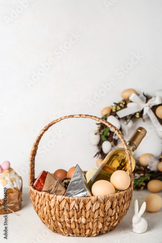 Basket with Easter eggs  bottle of wine and snacks on grey background