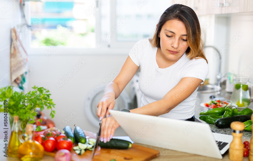 Nice latino woman planning to cook, looking for recipe on internet in her kitchen