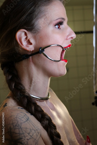 Devote BDSM Sklavin mit roten Lippen, roten Kontaktlinsen, Halsreif, Mundspreizer / Knebel und weit aufgerissenem Mund