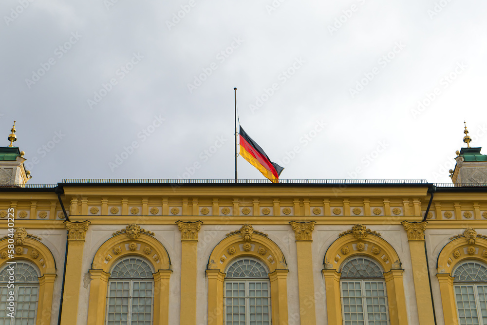 Obraz premium The flag of Germany is developing.The flag of Germany is on the building.The symbol of Germany.A beautiful building with a flag. Flag on the flagpole.Attraction.Old building.Government of Germany.sky.