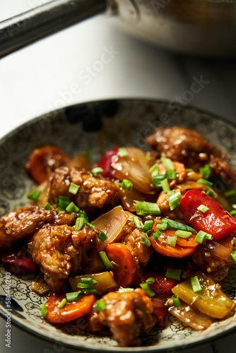 Chicken Manchurian in plate near wok where chicken was fried and cooked with sauce. 