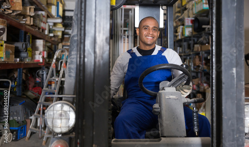 Cheerful Latin American worker of building materials warehouse working on forklift truck