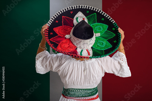 Woman shows Mexican hat with the colors of the Mexican flag. Mexican flag in background. photo