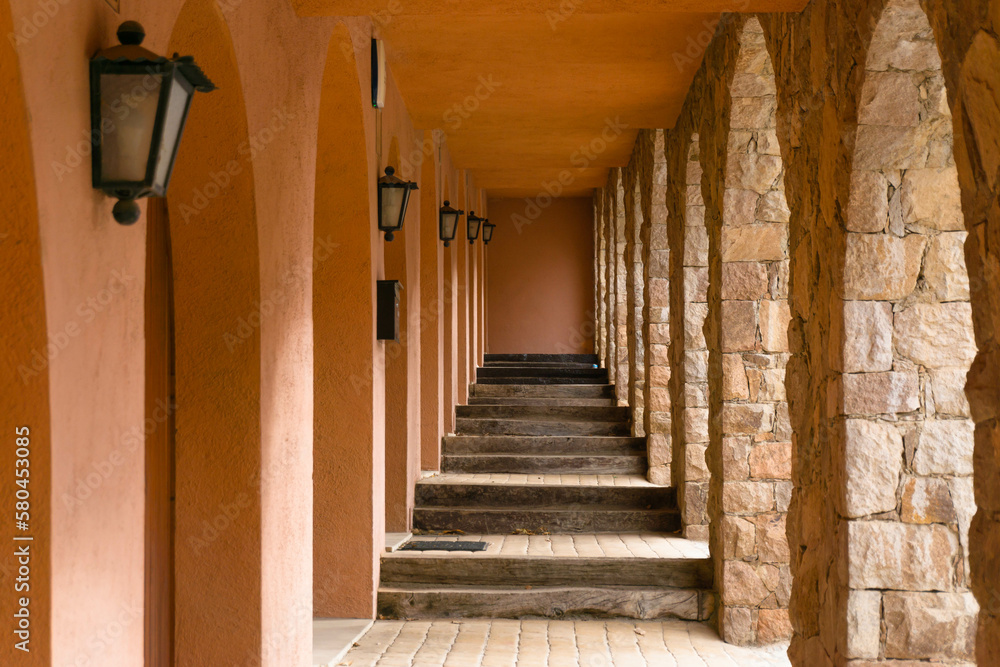 Long corridor with many arches on each side and in the center wooden stairs