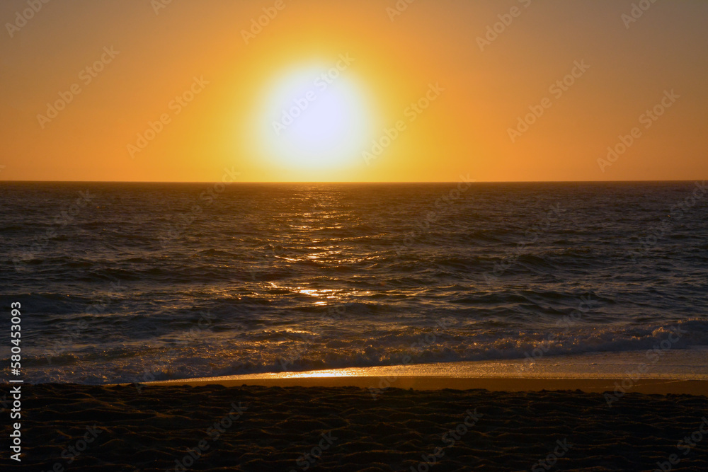 The bright evening sun sets over the horizon into the sea. Natural background from the beach