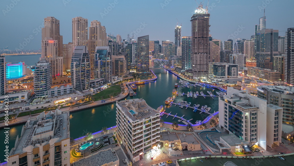 Naklejka premium Dubai Marina with several boat and yachts parked in harbor and skyscrapers around canal aerial day to night timelapse.
