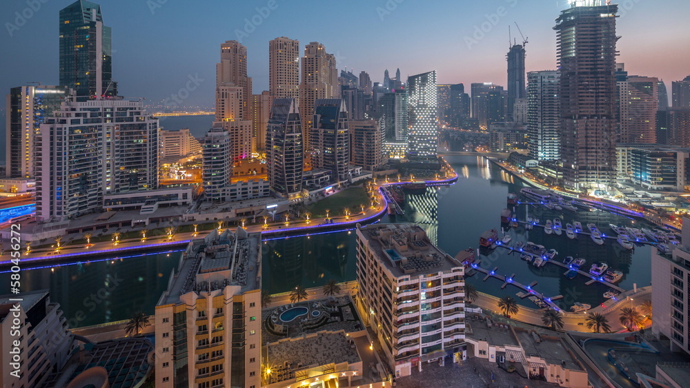 Obraz premium Dubai Marina with several boats and yachts parked in harbor and skyscrapers around canal aerial night to day timelapse.