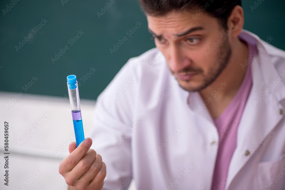 Young male chemistry teacher sitting in the classroom