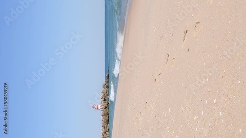 Vertical video of beach and lighthouse on jetty on Tavira Island, known as Ilha de Tavira in the Algarve in Portugal. 4K video with ocean sound.