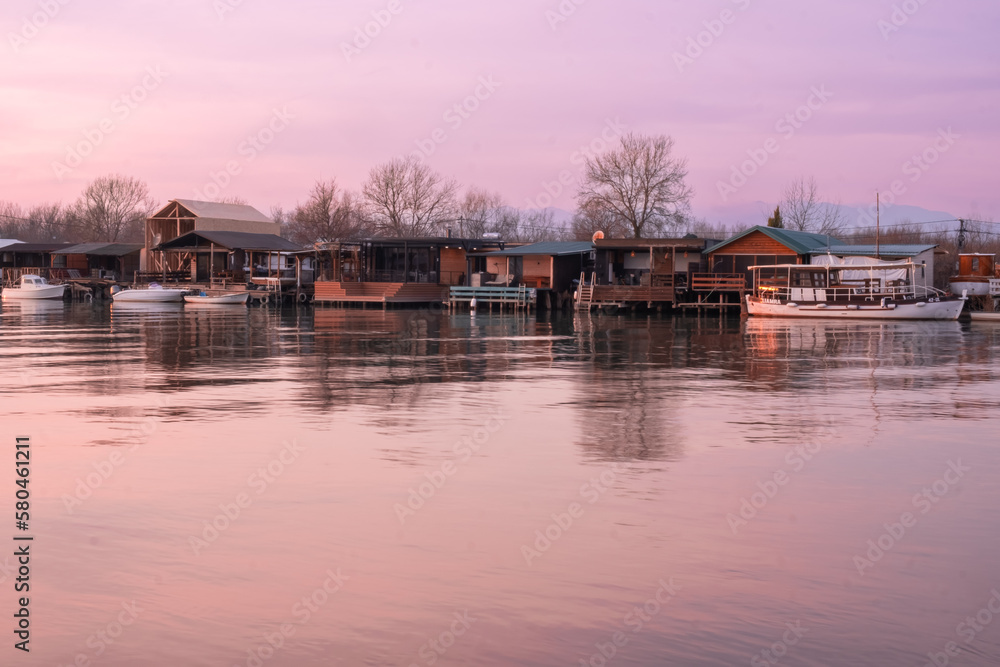 A purple sky is reflected in the water of a river with houses and a boat in the water.