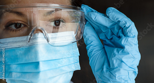 Photography portrait of a nurse or doctor dressed in work clothes and protective accessories, wearing goggles, blue latex gloves and a surgical mask