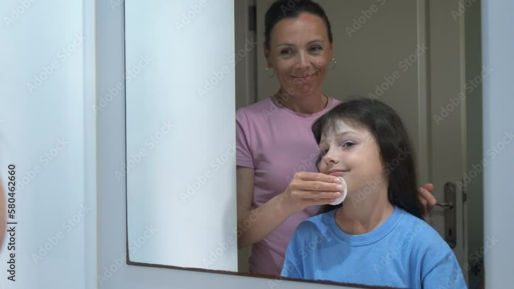 A mother teaches her daughter how to take care of her skin. Mom wipes her face with a lotion with a cotton pad to a beautiful girl. A mother teaches her daughter how to take care of her skin. Mom wipes her face with a lotion with a cotton pad to a beautiful girl.