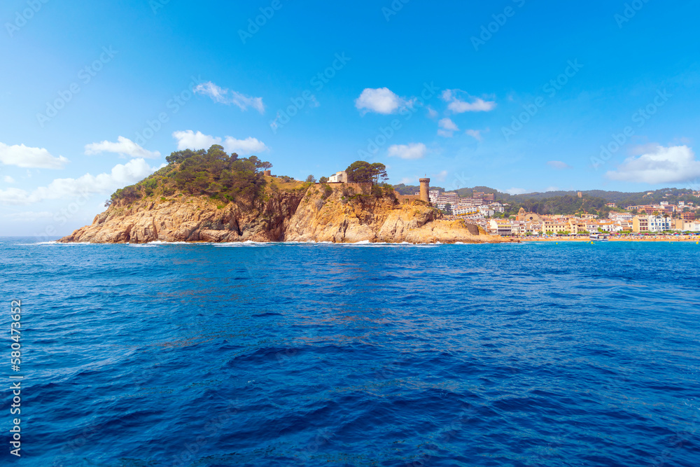View from the Mediterranean Sea of the beachfront Spanish town of Tossa de Mar, Spain, along the Costa Brava coast, with the tower of it's medieval castle and beach in view.