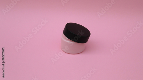 Envase de plástico para crema facial en color rosa con tapadera negra medio abierta.  photo