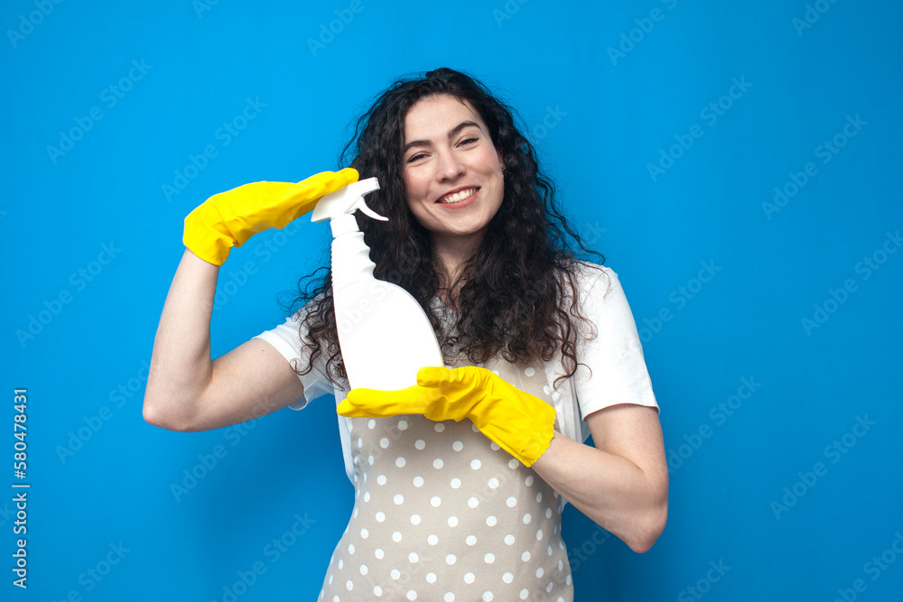 woman housewife in gloves holds detergent in her hands on blue background, woman cleaner advertises cleaning spray woman housewife in gloves holds detergent in her hands on blue background, woman cleaner advertises cleaning spray
