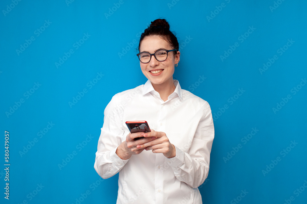 business woman manager in white shirt and glasses is typing on smartphone on blue background, girl office worker business woman manager in white shirt and glasses is typing on smartphone on blue background, girl office worker