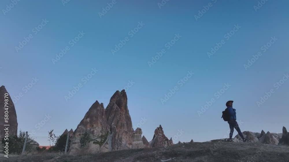 Traveler Girl With A Backpack And A Hat Wanders Among The Rocks Of Cappadocia, Aerial View Traveler Girl With A Backpack And A Hat Wanders Among The Rocks Of Cappadocia, Aerial View