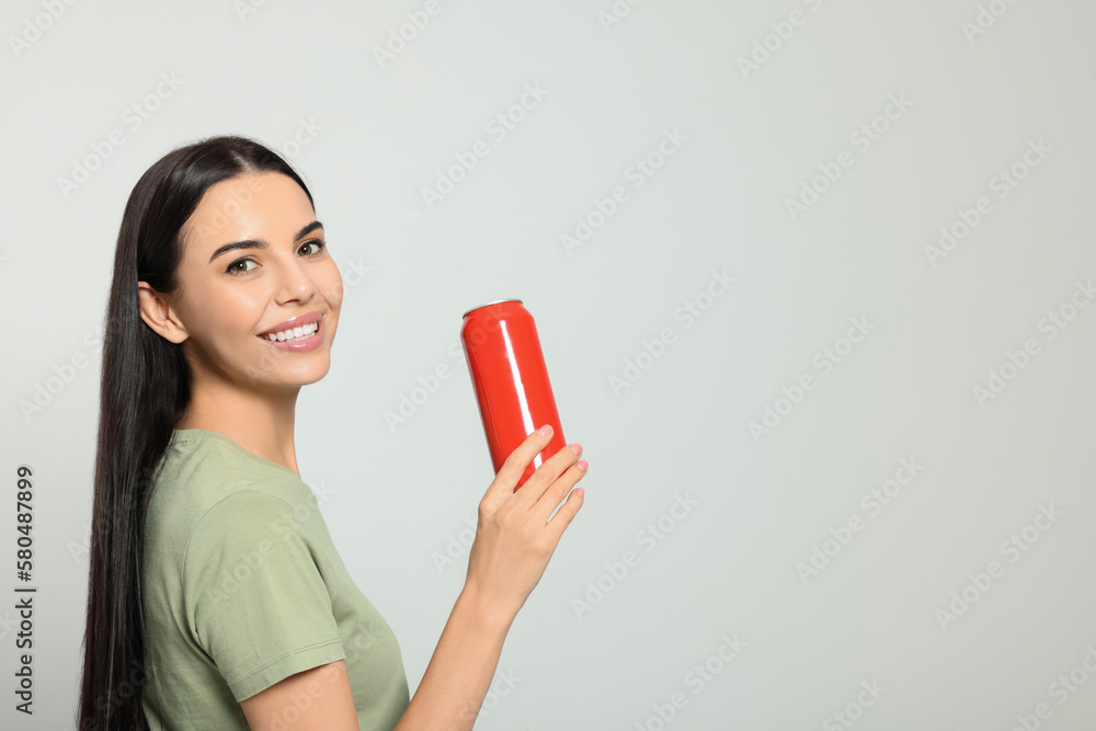 Beautiful happy woman holding red beverage can on light grey background. Space for text Beautiful happy woman holding red beverage can on light grey background. Space for text