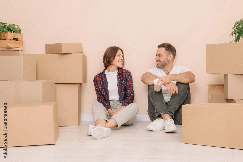 Happy couple with takeaway coffee resting on floor in new apartment. Moving day Happy couple with takeaway coffee resting on floor in new apartment. Moving day
