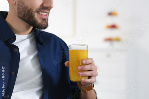 Man with delicious smoothie at home, closeup. Space for text