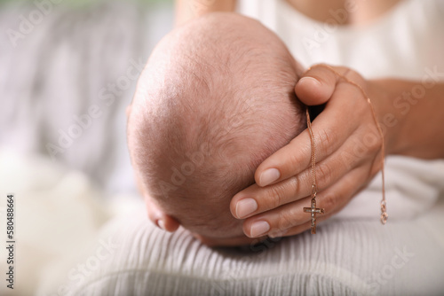 Mother holding newborn baby and Christian cross indoors, focus on hand