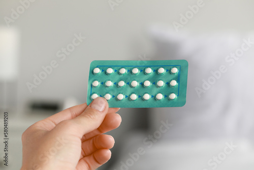 Woman holding blister of oral contraception pills against blurred background, closeup