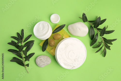 Different cosmetic products with olives and stones on light green background, flat lay