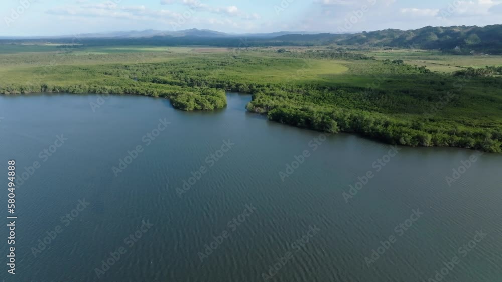 Aerial flyover tranquil bay water of Cano Hondo with green idyllic landscape and mountains in backdrop Aerial flyover tranquil bay water of Cano Hondo with green idyllic landscape and mountains in backdrop