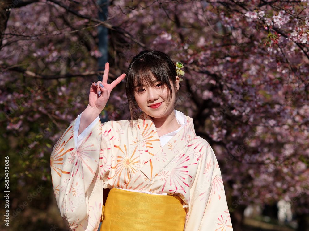 Portrait of beautiful young Chinese girl in Japanese kimono posing with blossom cherry flowers background in spring garden, beauty, emotion, lifestyle, expression and people concept. Portrait of beautiful young Chinese girl in Japanese kimono posing with blossom cherry flowers background in spring garden, beauty, emotion, lifestyle, expression and people concept.