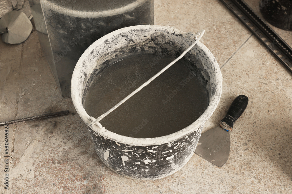 Bucket of adhesive mix and spatula on floor indoors Tiles installation process