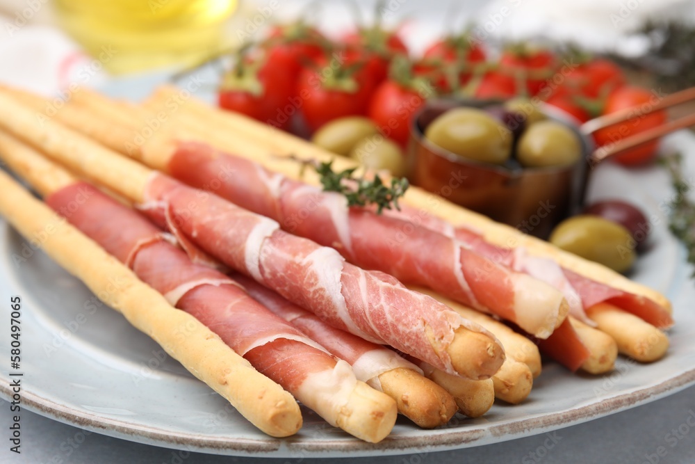 Delicious grissini sticks with prosciutto and snacks on white table, closeup Delicious grissini sticks with prosciutto and snacks on white table, closeup