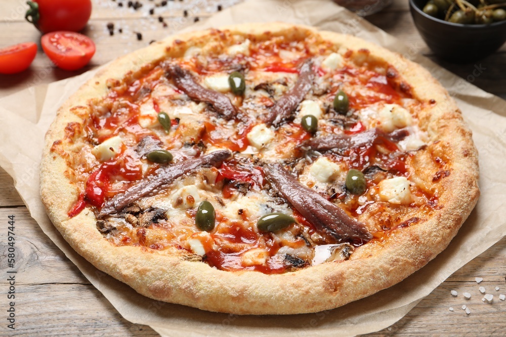 Tasty pizza with anchovies and ingredients on wooden table