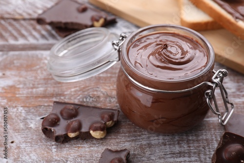 Jar with tasty paste and pieces of chocolate on wooden table, closeup