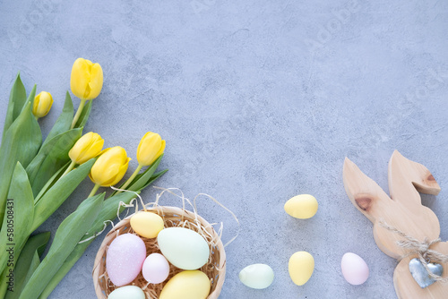 Yellow tulip bouquet with colorful easter eggs and rabbit on concrete background.